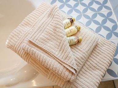 A stack of beige towels with small toiletry bottles on a tiled bathroom surface