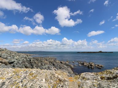 A rocky coastline with water and an island under a blue sky with clouds at Calac Cottage in Mousehole