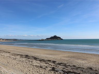 A sandy beach with seaweed by the shore and an island with a building in the sea at Calac Cottage in Mousehole