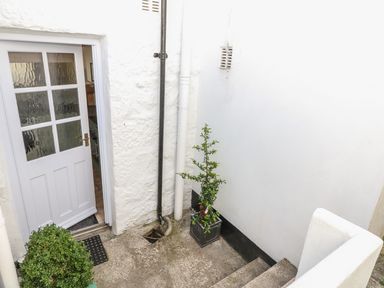 An outdoor area with a white door leading inside two potted plants a drain and steps at Calac Cottage in Mousehole