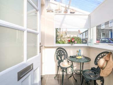 A small enclosed patio with metal chairs and table with decorative boats and flowers at Calac Cottage in Mousehole