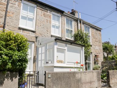 Exterior view of a stone house with white framed windows and a white enclosed porch at Calac Cottage in Mousehole