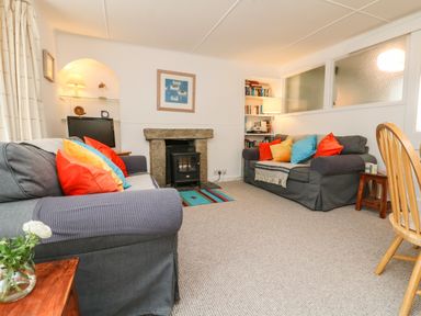 A living room with two sofas with colorful cushions a fireplace and bookshelves at Calac Cottage in Mousehole