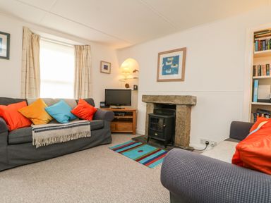 A living room with sofas cushions a fireplace a television and a bookshelf at Calac Cottage in Mousehole