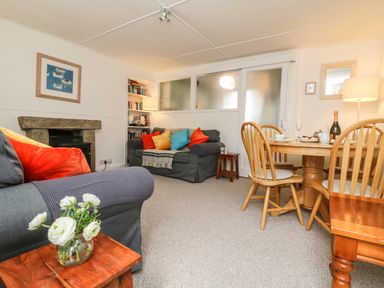 A living room with two sofas with colorful cushions a wooden dining table with chairs a small wooden side table with a vase of flowers and a fireplace at Calac Cottage in Mousehole