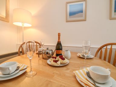 A dining table with cups saucers champagne glasses a bottle teapot plate of scones with jam and cream at Calac Cottage in Mousehole