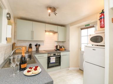 A kitchen with a sink stove oven refrigerator microwave and countertop with scones and a bottle of prosecco at Calac Cottage in Mousehole
