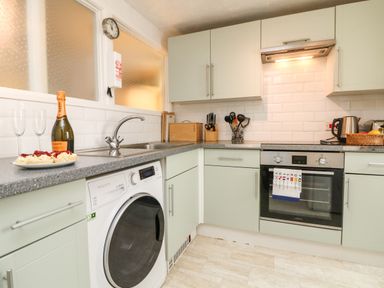 A kitchen with washing machine oven toaster kettle and cabinets at Calac Cottage in Mousehole