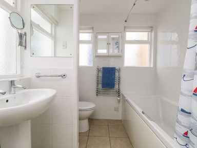 A bathroom with a sink a toilet a bathtub with a shower curtain and a towel rack at Calac Cottage in Mousehole
