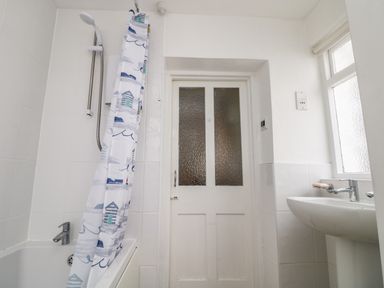 A bathroom with a bathtub shower combo a shower curtain a white door and a sink at Calac Cottage in Mousehole