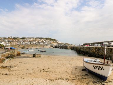 A sandy beach with a boat on shore and boats in water with houses and stone walls in the background at Calac Cottage in Mousehole