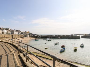 A harbor with small boats on water near a stone wall and buildings at Calac Cottage in Mousehole