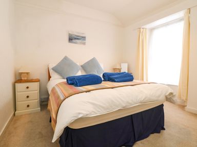 A bedroom with a bed with blue pillows and blue towels on a blanket with bedside tables and lamps at Calac Cottage in Mousehole