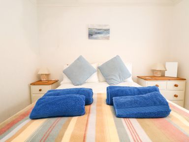 A bedroom with a double bed with two blue pillows and blue towels on a striped blanket at Calac Cottage in Mousehole