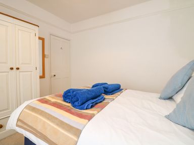 A bedroom with a bed with blue towels on a striped blanket and a white wardrobe on the left at Calac Cottage in Mousehole