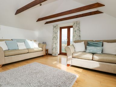 A living room with two beige sofas pillows and wooden beams at Castle Dore Barn in Fowey