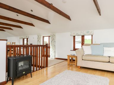 A living room with a beige sofa wooden side table windows and exposed wooden ceiling beams at Castle Dore Barn in Fowey