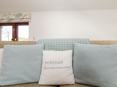 A sofa with blue and white cushions and a patterned throw near a window at Castle Dore Barn in Fowey
