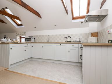 A kitchen with white cabinets wooden countertops a microwave kettle toaster and skylights at Castle Dore Barn in Fowey