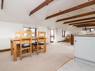 A dining area with wooden table and chairs under a ceiling with exposed beams at Castle Dore Barn in Fowey