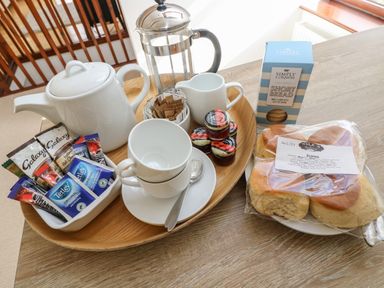A wooden tray with a teapot cups spoons jam small milk jug tea bags and a French press next to a plate with scones and a box of shortbread at Castle Dore Barn in Fowey