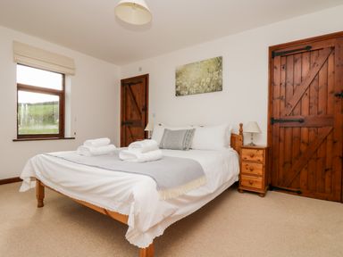 A bedroom with a wooden bed and bedside table with lamps and folded towels on the bed at Castle Dore Barn in Fowey