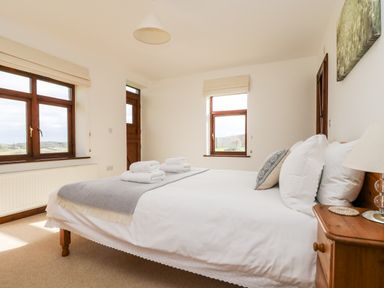 A bedroom with a double bed white bedding folded towels wooden bedside table and windows at Castle Dore Barn in Fowey