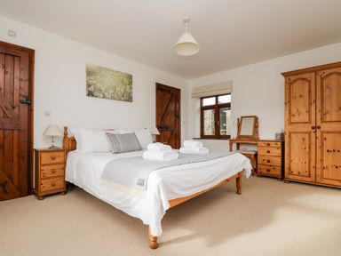 A bedroom with a wooden bed, bedside tables, wardrobe, and dressing table at Castle Dore Barn in Fowey