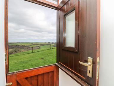 A half open wooden door with a window showing a green field and cloudy sky at Castle Dore Barn in Fowey
