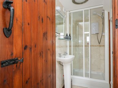 A small bathroom with a wooden door a white pedestal sink and a glass shower enclosure at Castle Dore Barn in Fowey