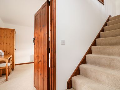 A staircase with carpet and wooden banister next to an open wooden door leading to a room with a wooden desk and wardrobe at Castle Dore Barn in Fowey