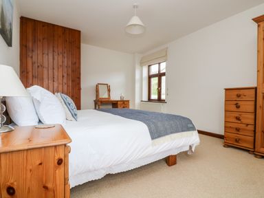 A bedroom with a bed a bedside table with a lamp a dressing table a window and wooden furniture at Castle Dore Barn in Fowey