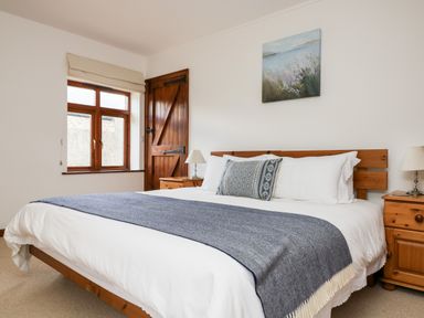 A bedroom with a wooden bed and bedside tables with lamps at Castle Dore Barn in Fowey