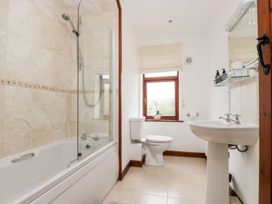 A bathroom with a bathtub shower combination a toilet a sink a window and a mirror at Castle Dore Barn in Fowey