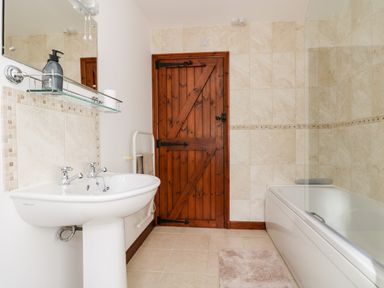 A bathroom with a white sink a wooden door a bathtub and tiled walls at Castle Dore Barn in Fowey