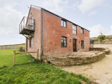 A two-story brick house with several windows a small balcony and a stone wall outside at Castle Dore Barn in Fowey