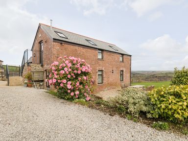 A brick house with a slate roof and outdoor seating area surrounded by bushes and flowers at Castle Dore Barn in Fowey
