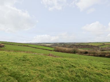 A rural landscape with green fields and a partly cloudy sky at Castle Dore Barn in Fowey