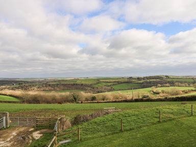 A rural landscape with green fields cows fences and cloudy sky at Castle Dore Barn in Fowey