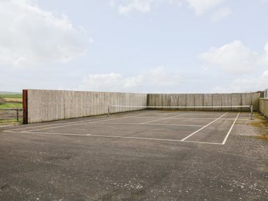 An outdoor tennis court with a net and concrete walls at Castle Dore Barn in Fowey