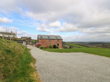 A gravel driveway leading to a brick building with skylights and surrounding greenery at Castle Dore Barn in Fowey
