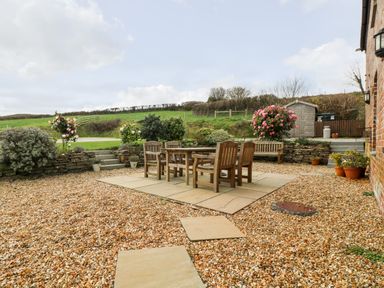 An outdoor patio area with wooden table and chairs surrounded by gravel and plants at Castle Dore Barn in Fowey