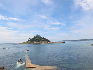 A small island with a castle and buildings surrounded by water and boats at Surfside in Marazion
