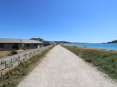 A gravel path with stone buildings on the left and a beach with water on the right at Surfside in Marazion