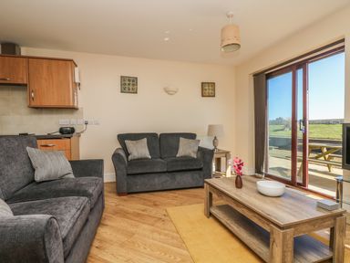 A living room with two sofas a wooden coffee table with a vase and bowl a side table with a lamp and sliding glass doors leading outside at Surfside in Marazion