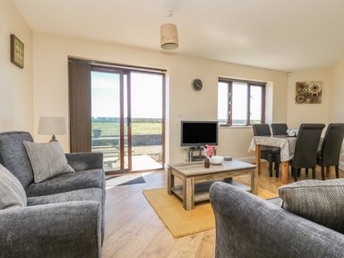 A living room with two grey sofas a wooden coffee table a TV and a dining table with six black chairs at Surfside in Marazion