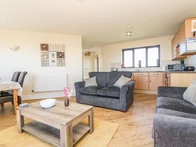 A living room with gray sofas wooden coffee table and kitchen area at Surfside in Marazion