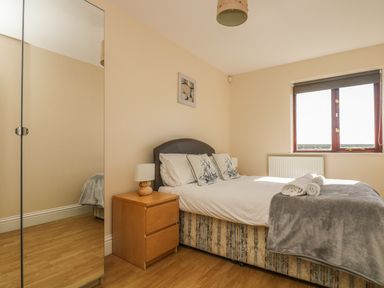 A bedroom with a double bed two pillows a bedside table with a lamp a window and a wardrobe at Surfside in Marazion
