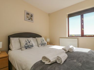 A bedroom with a double bed with ship print pillows and rolled towels on the bed by a window at Surfside in Marazion