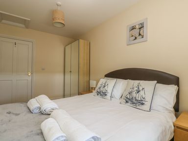 A bedroom with a bed with nautical pillows towels on bed a wardrobe and a framed picture on the wall at Surfside in Marazion